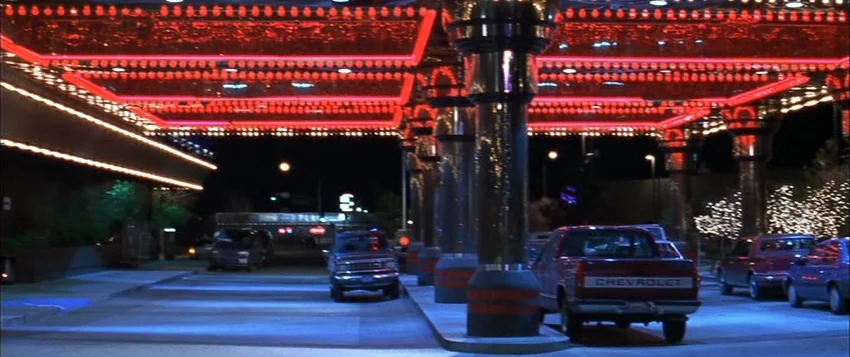Hard Eight (1996) movie still: establishing — A hotel porte cochere illuminated by extensive red neon tubing at night. Several parked cars occupy…