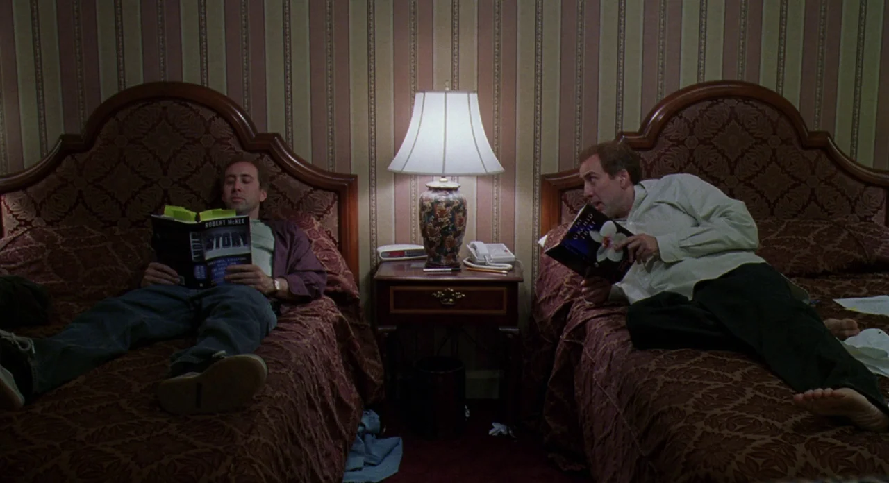 Adaptation (2002) movie still: wide — A hotel room features two beds separated by a wooden nightstand with a lamp. Both men lie on their backs…