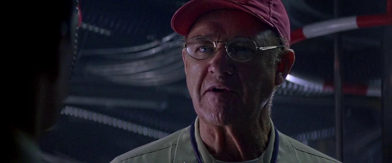 Crimson Tide (1995) movie still: closeup — A dark industrial environment with overhead piping and machinery visible in the background. An elderly…