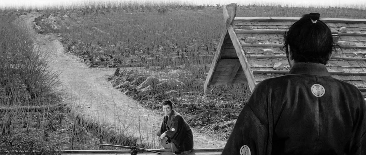 Yojimbo (1961) movie still: wide — A rural landscape with a dirt path running through harvested fields and tall grasses. Two men in traditional…