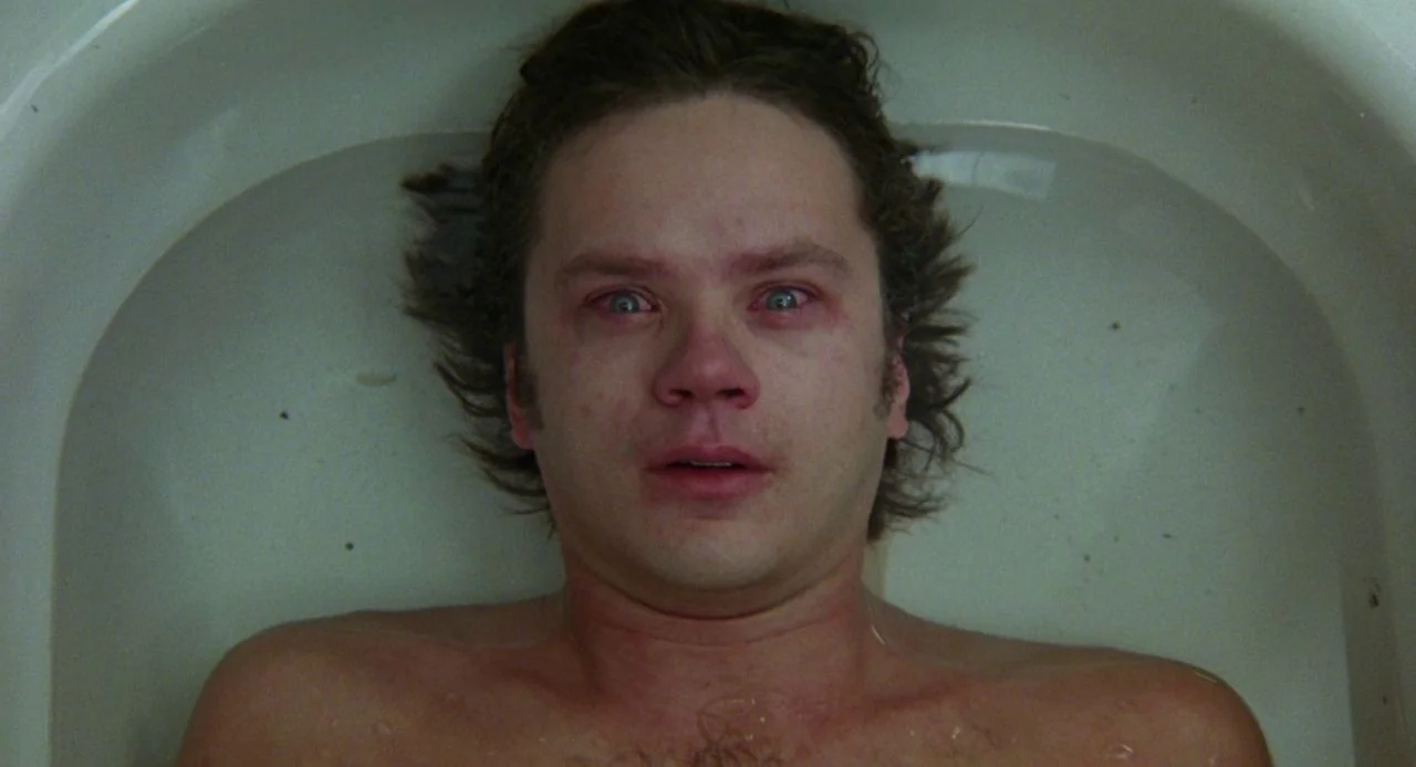 Jacob’s Ladder (1990) movie still: closeup — A man reclines in an off-white porcelain bathtub filled with clear water. He looks directly upward at…