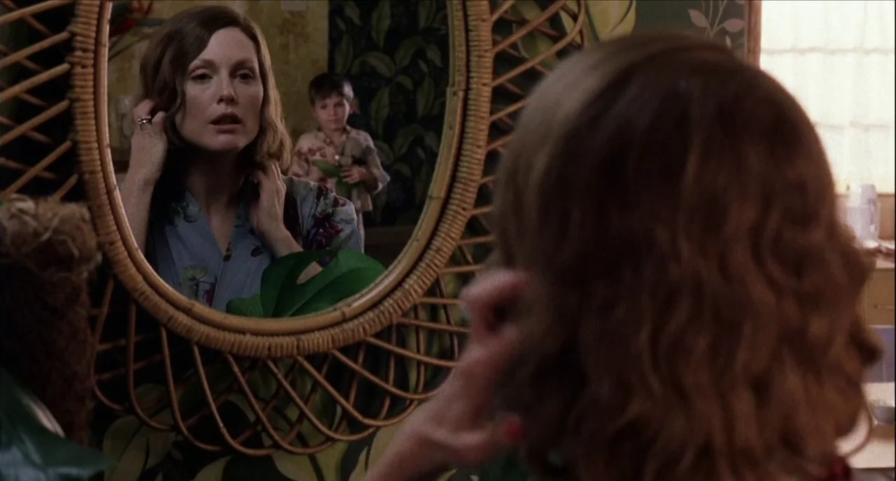The Hours (2002) movie still: medium — A dressing area features a large round rattan-framed mirror with leafy wallpaper background. A woman in a…