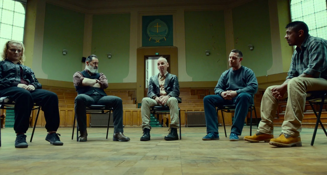 T2 Trainspotting (2017) movie still: fullbody — A spacious hall with tall windows and wood paneling hosts a group meeting. Five people sit on…