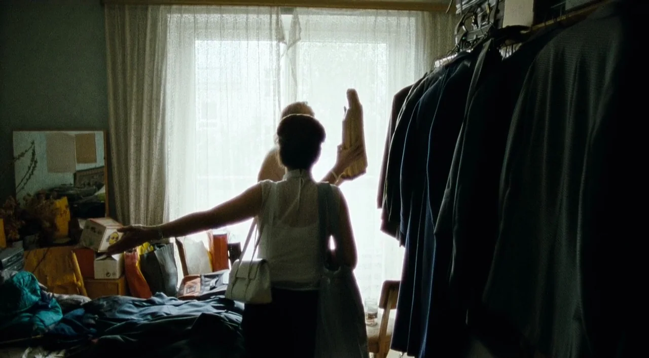 Paradise: Faith (2012) movie still: medium — An interior bedroom with clothing racks and clutter bathed in light from a window. A woman stands in…