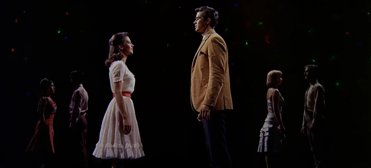 West Side Story (1961) movie still: fullbody — A dark space with scattered points of light in the background. Two central figures face each other…