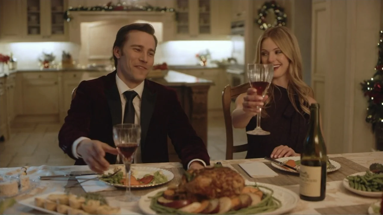 Driving Madeleine (2022) movie still: medium — A well-lit room contains a dinner table set for a holiday meal with a roast chicken. A man in a…