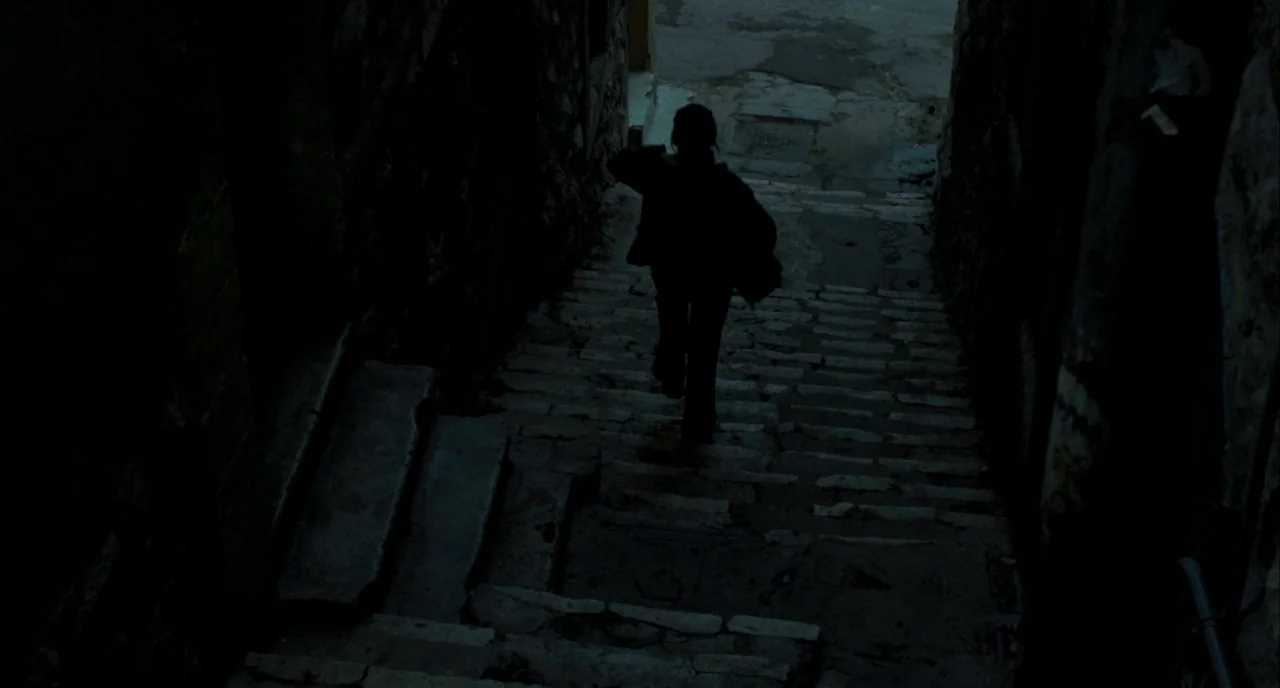 Incendies movie still: fullbody — A dark, narrow stone staircase descends between two rough masonry walls. A solitary silhouette descends the steps…
