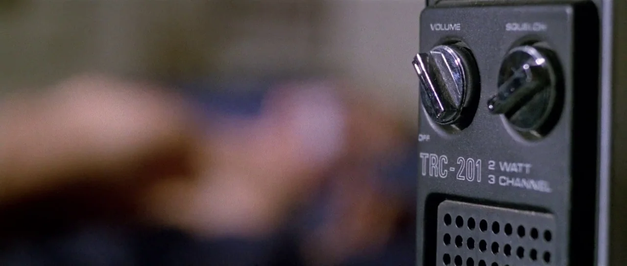 The New York Ripper (1982) movie still: closeup — A close-up view shows a black portable two-way radio with white control lettering. The background…