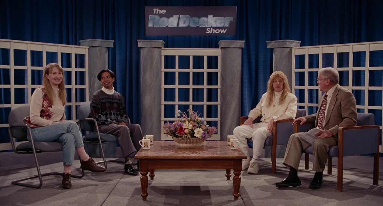 Gentlemen Broncos (2009) movie still: wide — A television talk show set with a blue curtain background and white lattice panels. Four guests and a…