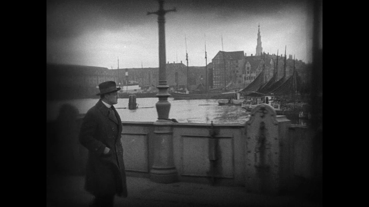 Master of the House (1925) movie still: fullbody — A stone bridge overlooks a harbor featuring moored boats and industrial buildings in distance. A…