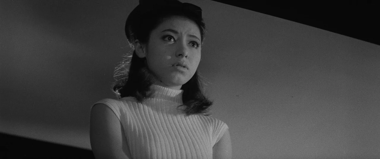 Carmen From Kawachi (1966) movie still: medium — An interior space with a dark, minimalist background wall behind the subject. A woman looks…