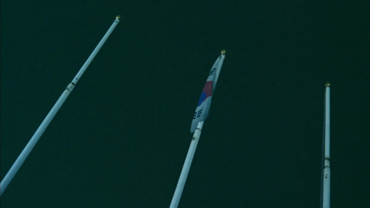 Whispering Corridors (1998) movie still: wide — Three thin metal poles stand against a deep, dark, featureless night sky. A South Korean flag hangs…