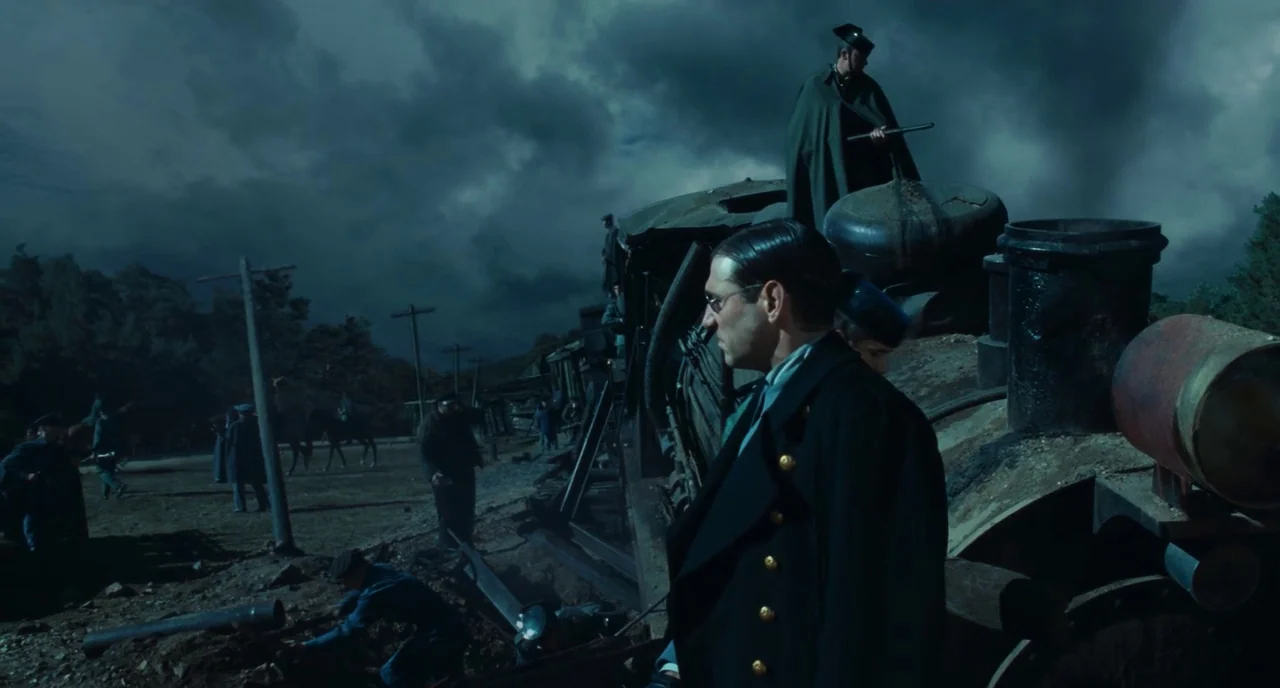 Pan’s Labyrinth (2006) movie still: medium — An overturned train engine sits in a dirt clearing beneath a stormy grey sky. A man in a dark coat…