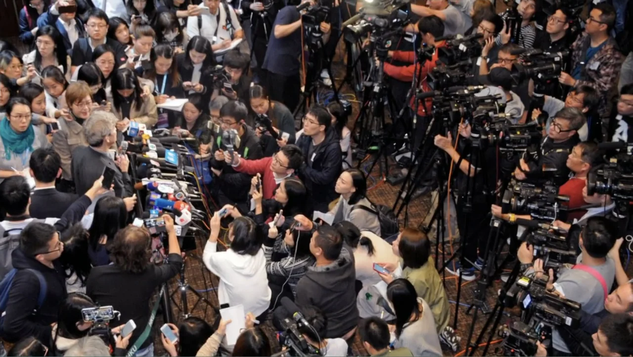 Almost Human: Rise of the Apes (2022) movie still: wide — A dense gathering of media personnel fills an indoor conference space with professional…