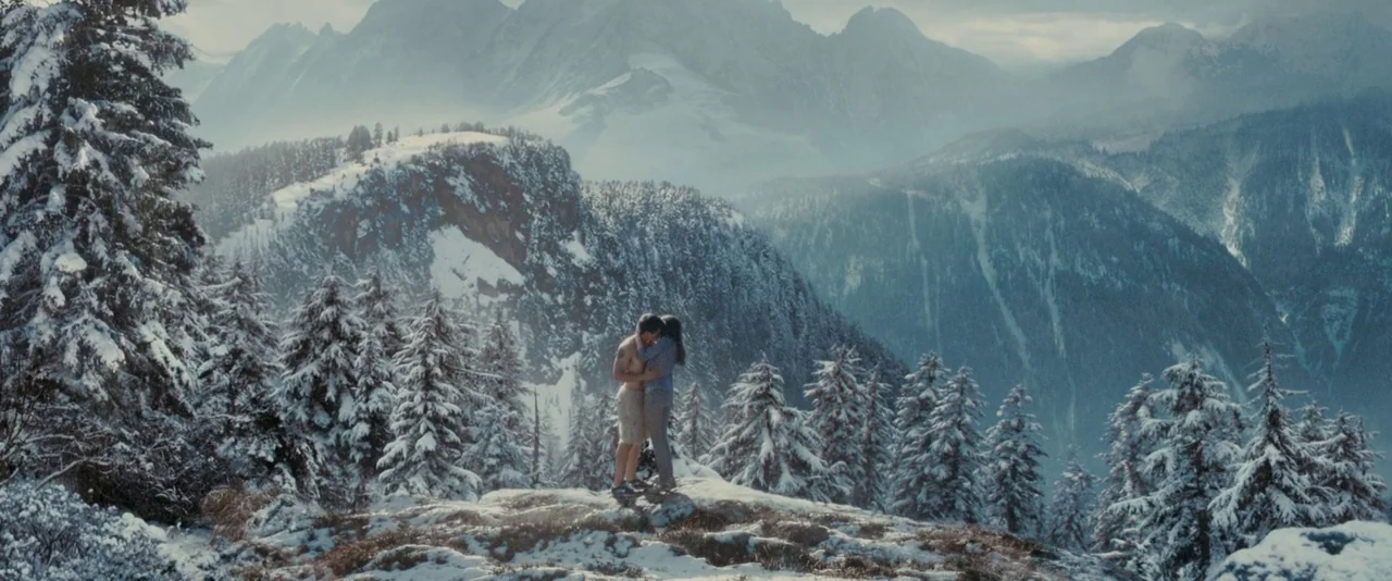 The Twilight Saga: Eclipse (2010) movie still: wide — Two people embrace on a rocky outcrop surrounded by a vast, snow-covered mountain range. The…