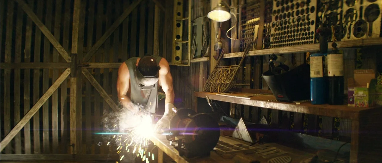 Magic Mike XXL (2015) movie still: medium — A cluttered workshop with wood-paneled walls and metal shelves filled with tools and parts. A man in a…