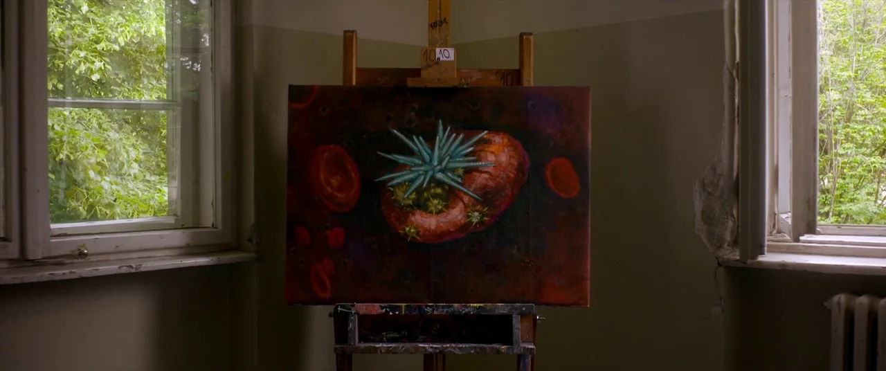 Mayhem (2017) movie still: medium — A wooden easel holds a dark red painting in a room with two windows. The room has neutral-toned walls and views…
