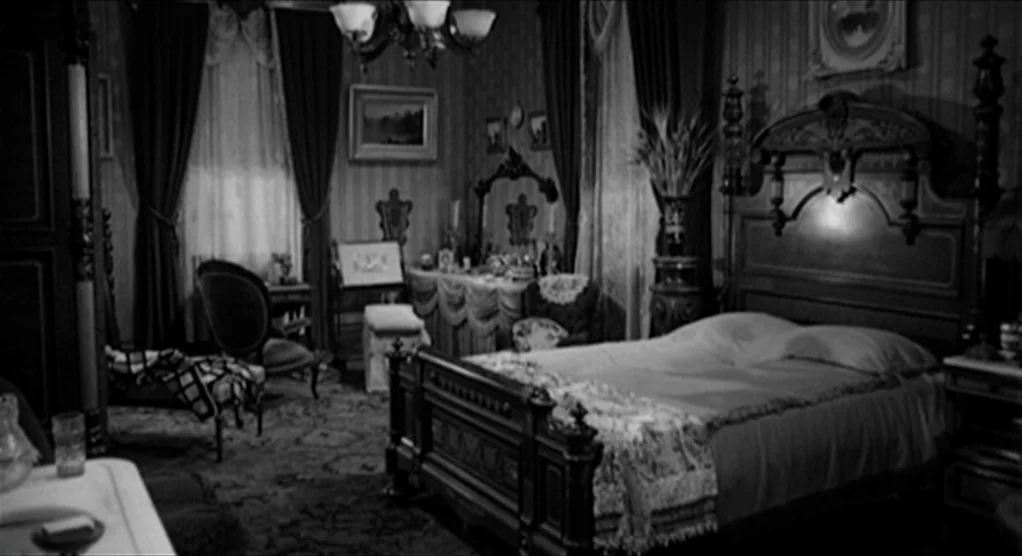 Psycho movie still: wide — A dark, heavily furnished 1940s room features a large wooden bed and ornate furniture. The space contains patterned…