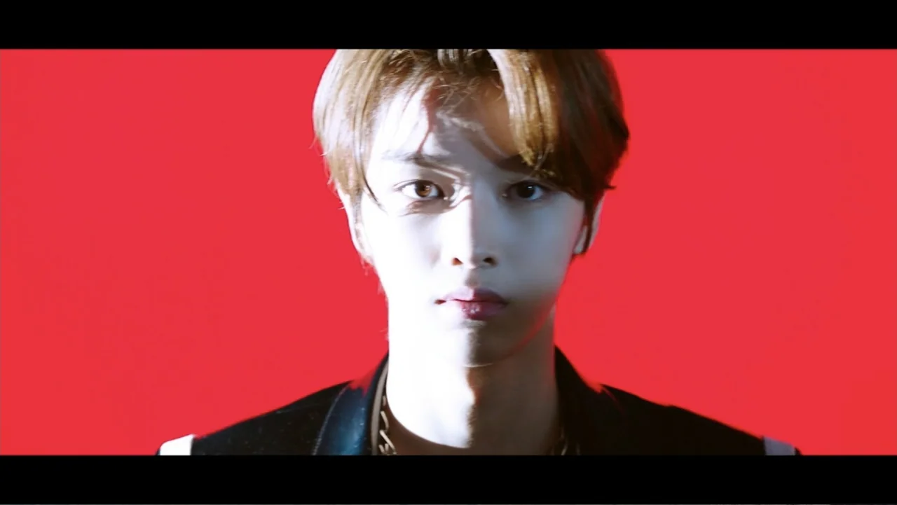 Lee Soo Man: King of K-Pop (2025) movie still: closeup — A person is centered against a flat, vibrant red background. The subject faces the camera…