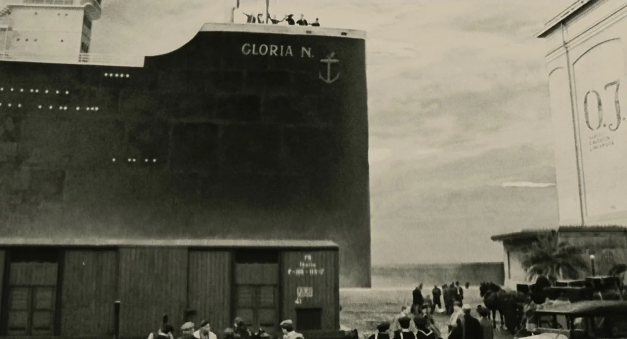And The Ship Sails On (1983) movie still: wide — A massive ocean liner named Gloria N. towers over a crowded industrial shipping dock. People mill…