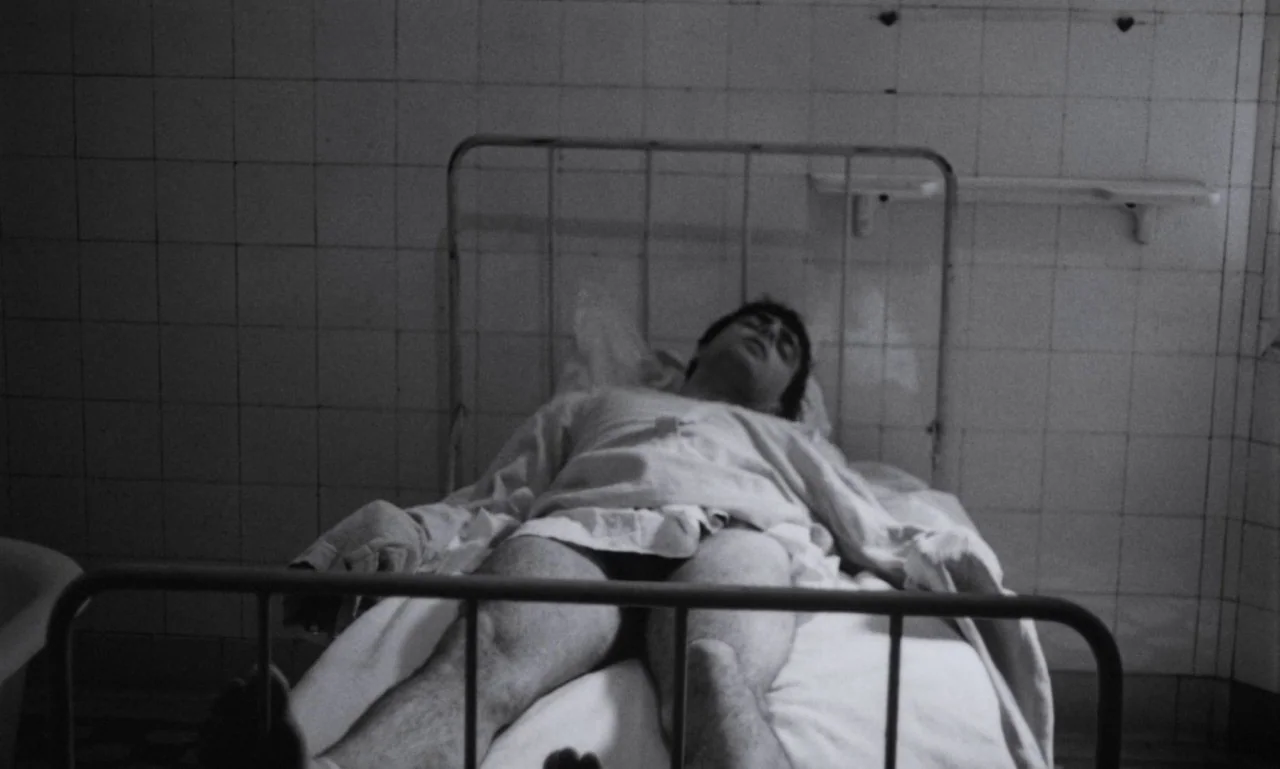 The Secret Son (1979) movie still: medium — A hospital room features tiled walls and a metal-framed bed with white linens. A young man with dark…