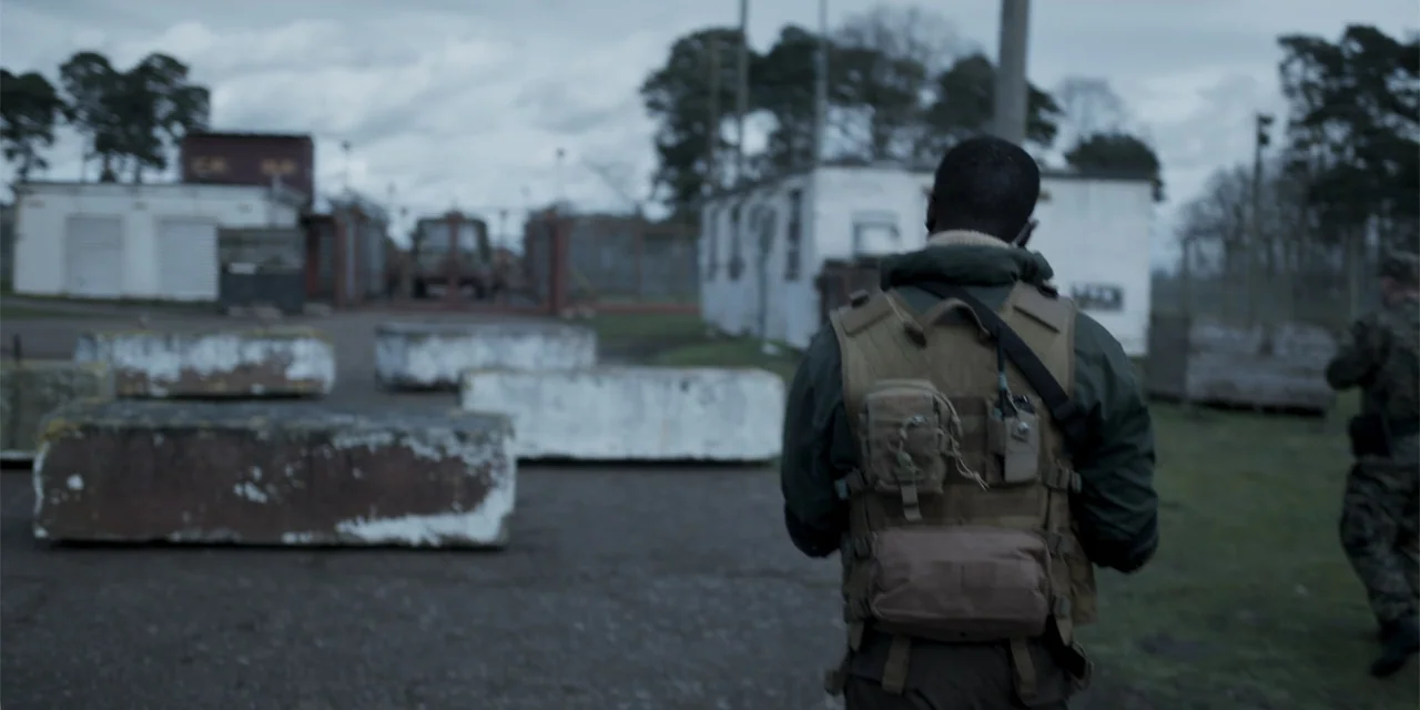 Mi última bala (1998) movie still: medium — An outdoor military facility features concrete barriers and white prefabricated structures under gray…