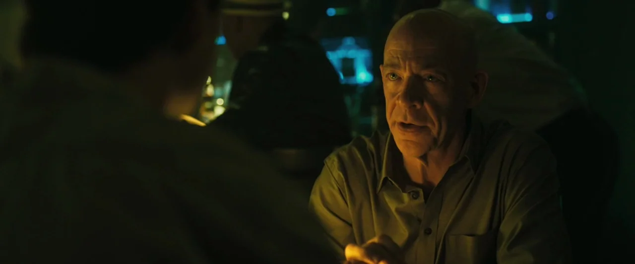 Whiplash (2014) movie still: medium — A dimly lit booth with blurred patrons in the background and glowing digital screens. An older man sits at the…
