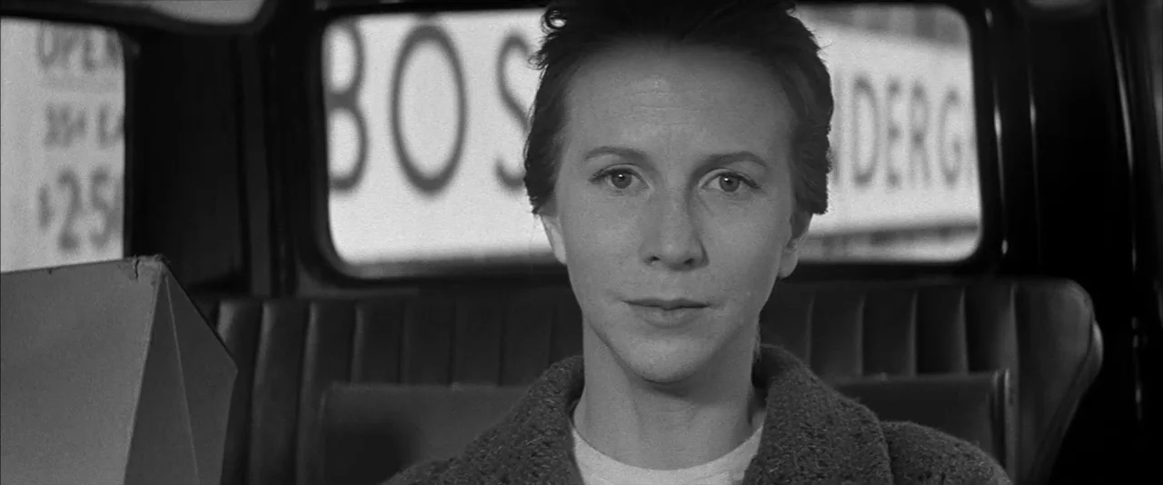 The Haunting (1963) movie still: closeup — The interior of a car with a view of a city window advertisement behind. A woman sits in the passenger…