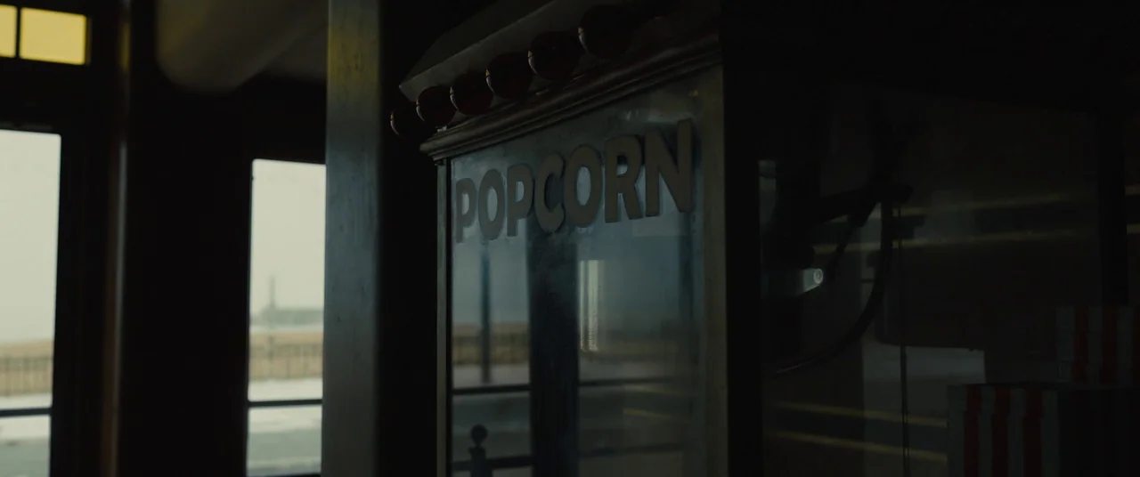 Empire of Light (2022) movie still: closeup — A close view of a glass popcorn machine featuring prominent lettering in a room. Through the nearby…