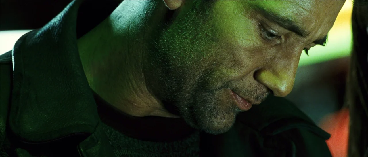 Shoot 'Em Up (2007) movie still: closeup — A close view inside a dimly lit vehicle during the night. A man with dark stubble looks downward while…
