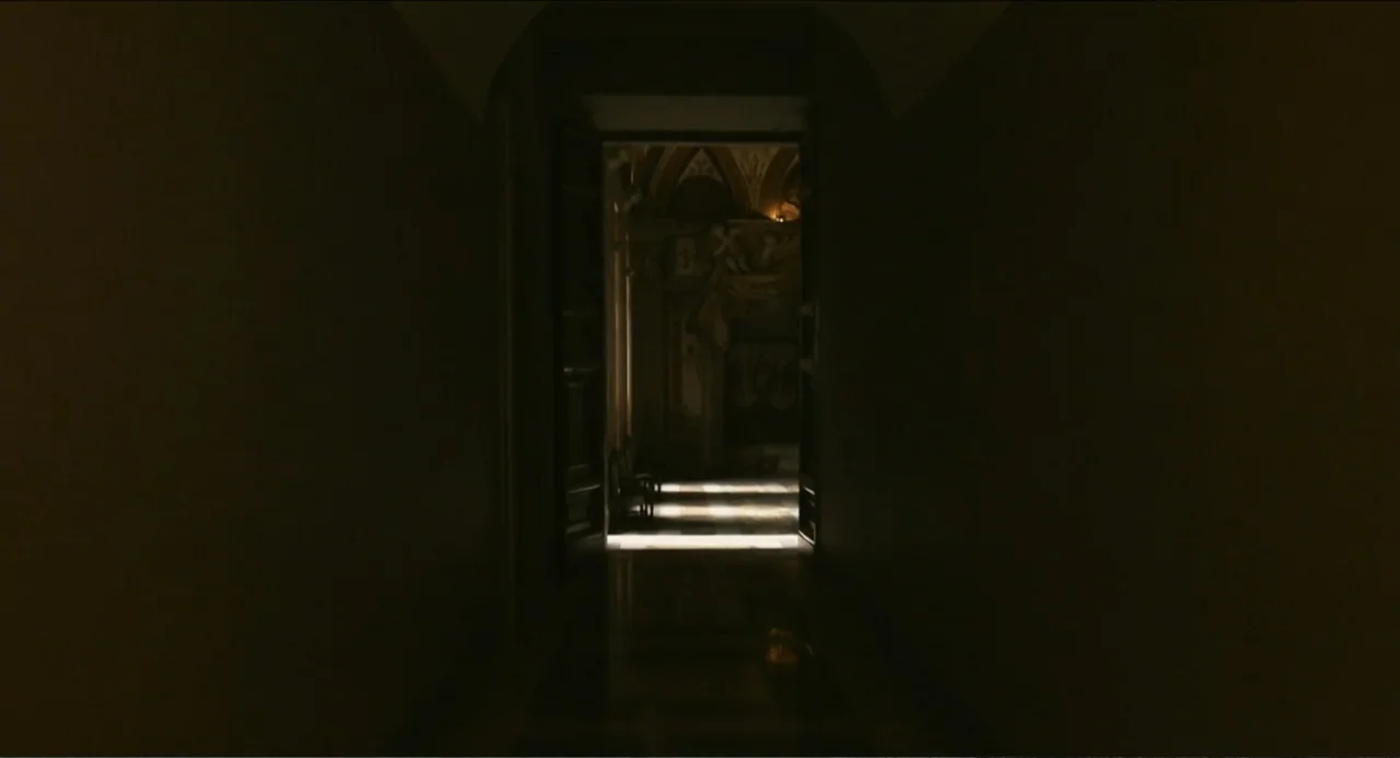 Pope Francis: A Man of His Word (2018) movie still: establishing — A dark, narrow stone hallway leads into an brightly illuminated room with marble…