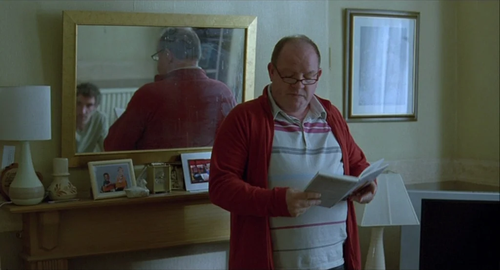 Looking for Eric (2009) movie still: medium — A residential room features a wooden mantelpiece adorned with small framed photographs and a lamp. An…