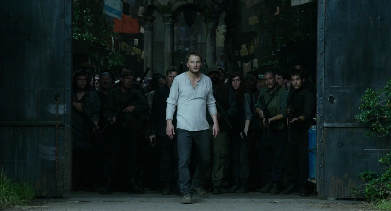 Dawn of the Planet of the Apes (2014) movie still: fullbody — A group of armed individuals walks through large industrial iron gates into an open…