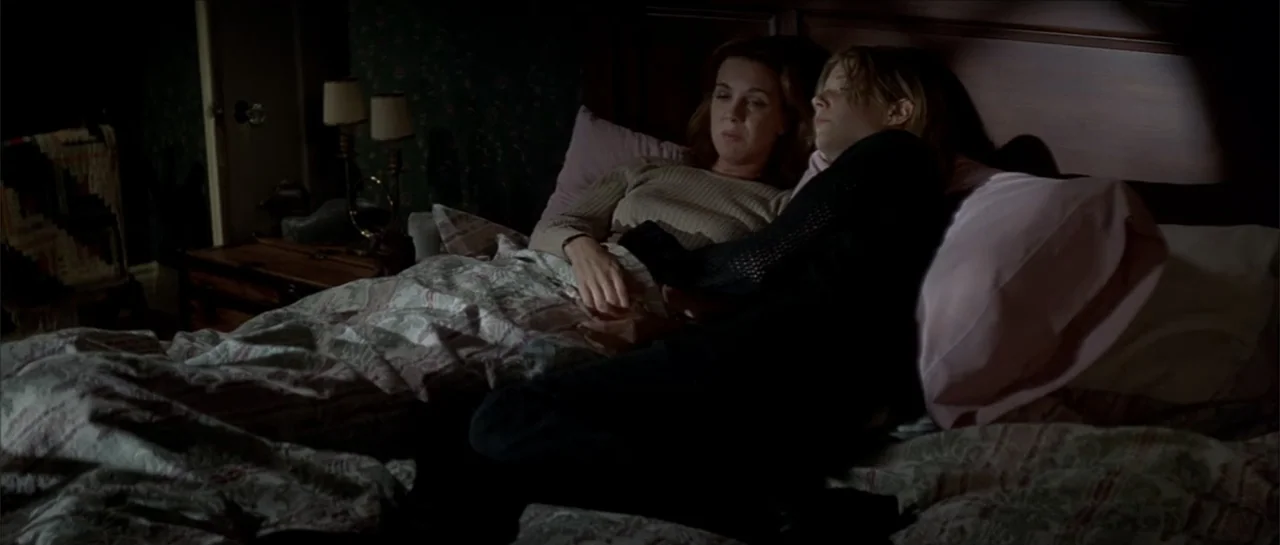 Moonlight and Valentino (1995) movie still: medium — A dark bedroom with patterned bedding and a wooden headboard. Two women lie side by side in bed…