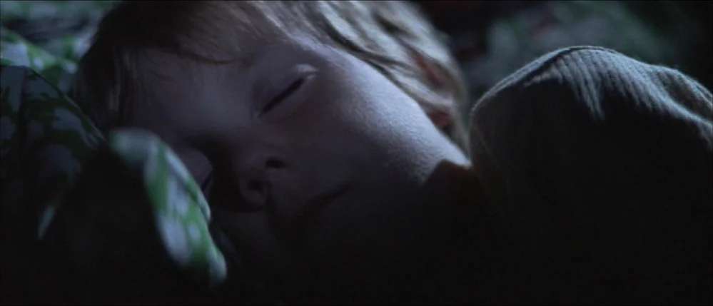 Close Encounters Of The Third Kind (1977) movie still: closeup — A young child sleeps in a dark room under patterned green sheets. The subject is…
