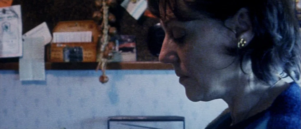 Wonderland (1999) movie still: closeup — A cluttered wall featuring pinned papers and hanging items serves as the background. A woman is positioned…