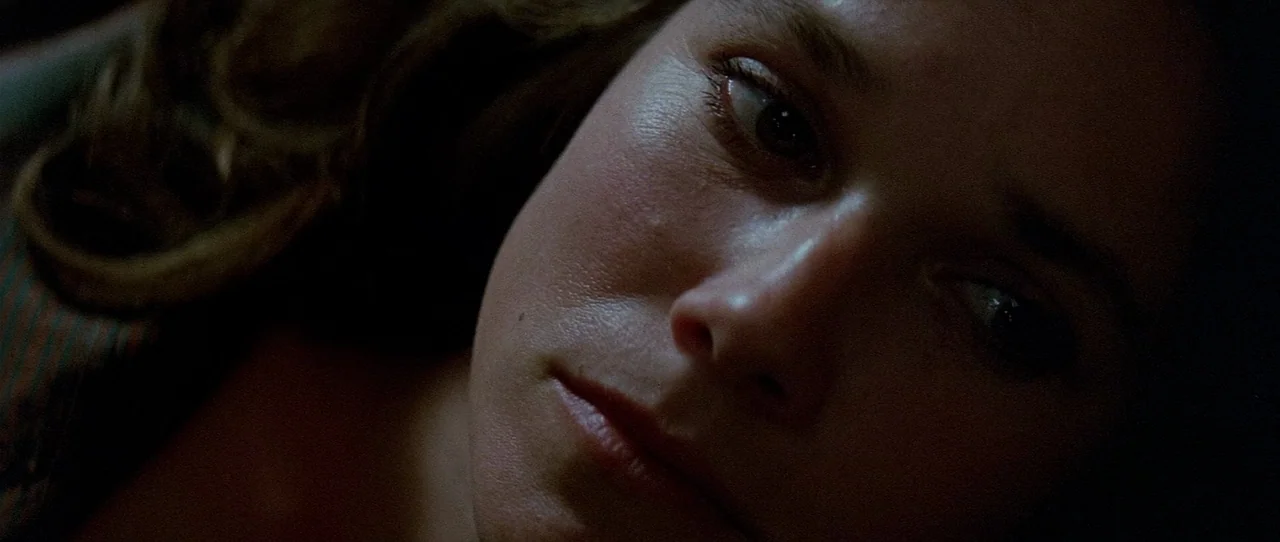 The Entity (1982) movie still: closeup — A close-up view of a woman lying down in a dark room. The subject gazes toward the side of the frame while…