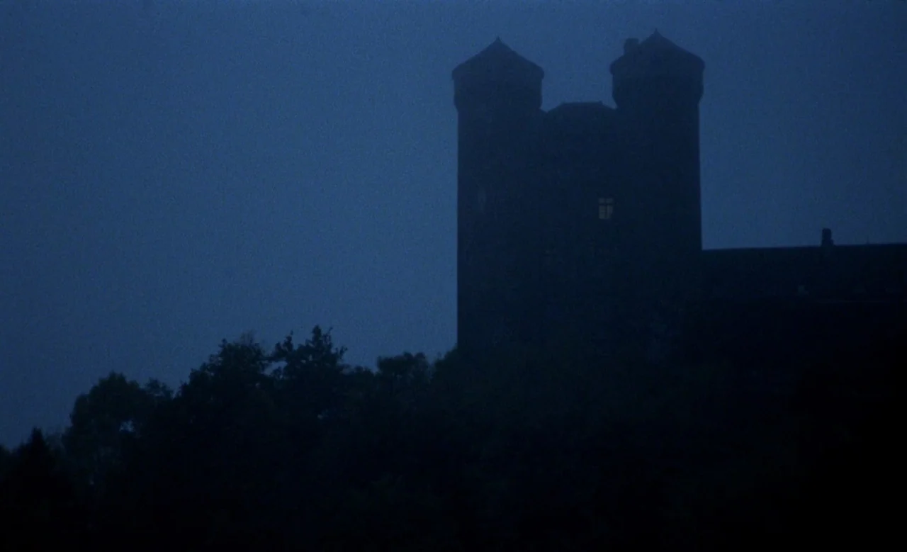 Blanche (1971) movie still: establishing — A stone castle with twin towers looms over a dark, silhouetted tree line at night. A single window in the…