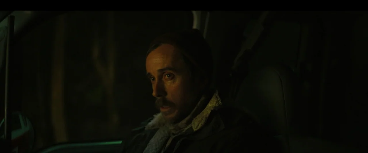 Wolf Man (2025) movie still: closeup — A dark car interior at night with a single man in the driver seat. The man wears a jacket with shearling…