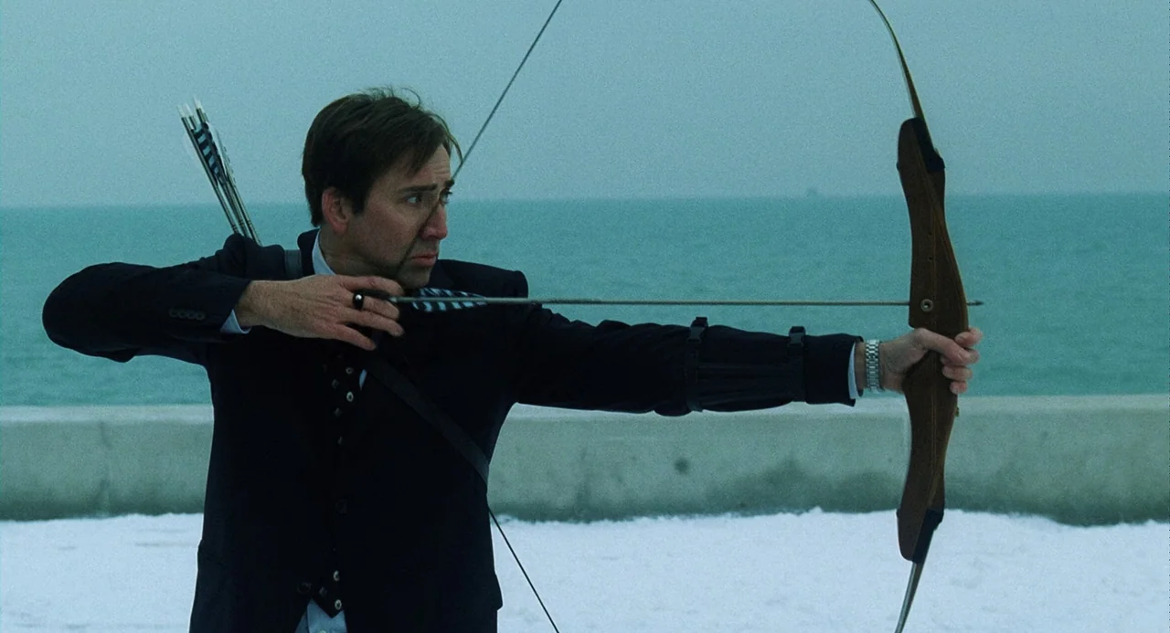 The Weather Man (2005) movie still: medium — A man stands on a snowy shoreline overlooking a calm sea during an overcast day. He aims a wooden…