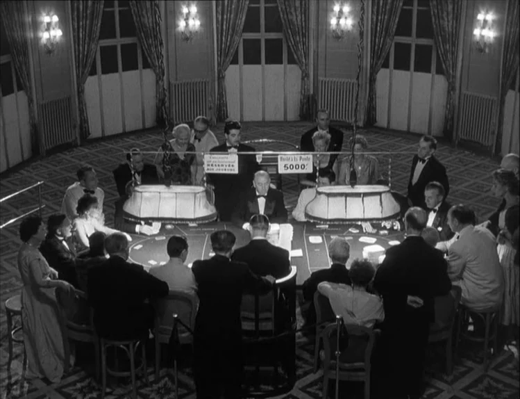 Bob le Flambeur (1956) movie still: wide — A high-angle view of a formal casino room with multiple card tables and occupants. The room features…