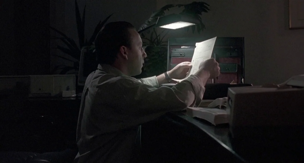 Three Colours: White (1994) movie still: medium — A darkened workspace at night featuring a desk lamp and a briefcase. A man sits at the desk while…