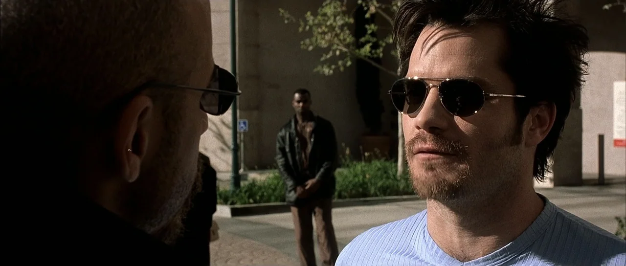 A Man Apart (2003) movie still: medium — An outdoor paved plaza with a building facade and small patch of green landscaping. A man in a blue shirt…