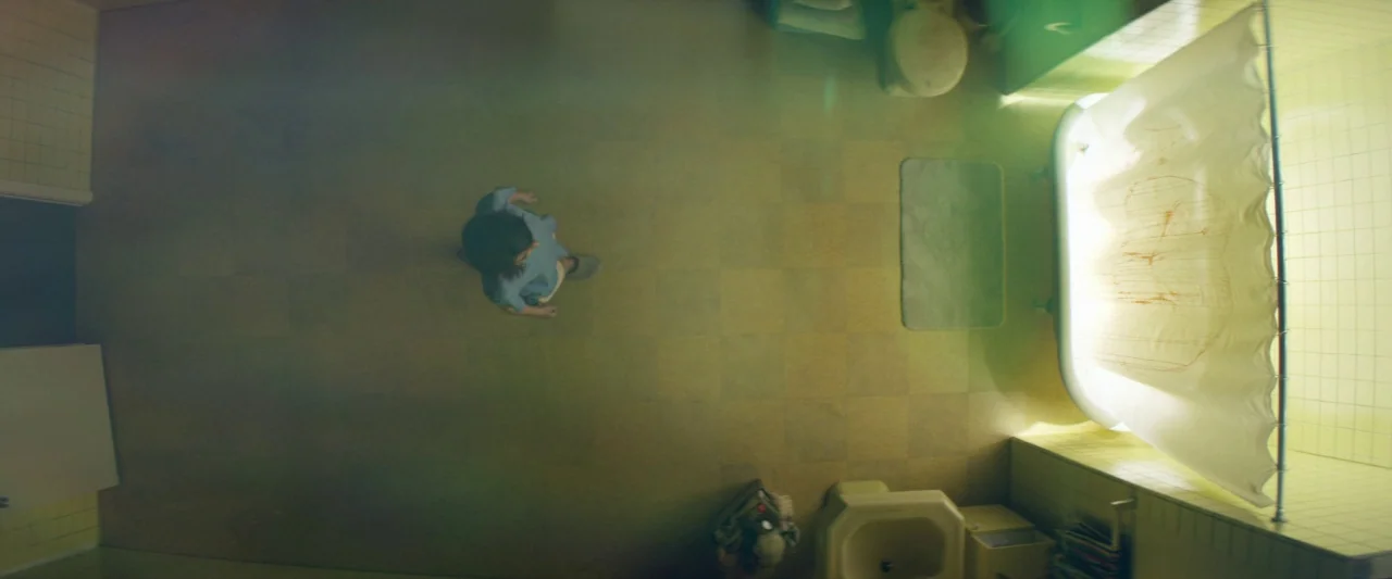 Seven Stages to Achieve Eternal Bliss (2018) movie still: wide — A spacious room features yellow tiled walls and a bathtub with a closed curtain. A…