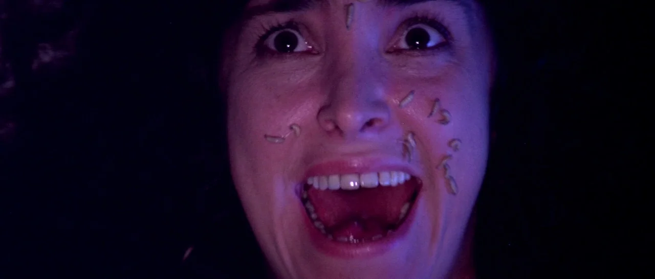 Suspiria (1977) movie still: closeup — A person's face is shown in extreme close-up against an entirely black background. Several white maggots…