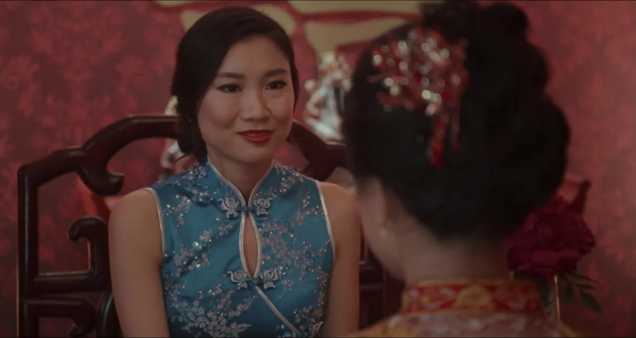 Five Blind Dates (2024) movie still: medium — An interior space features deep red patterned wallpaper behind two individuals sitting together. A…