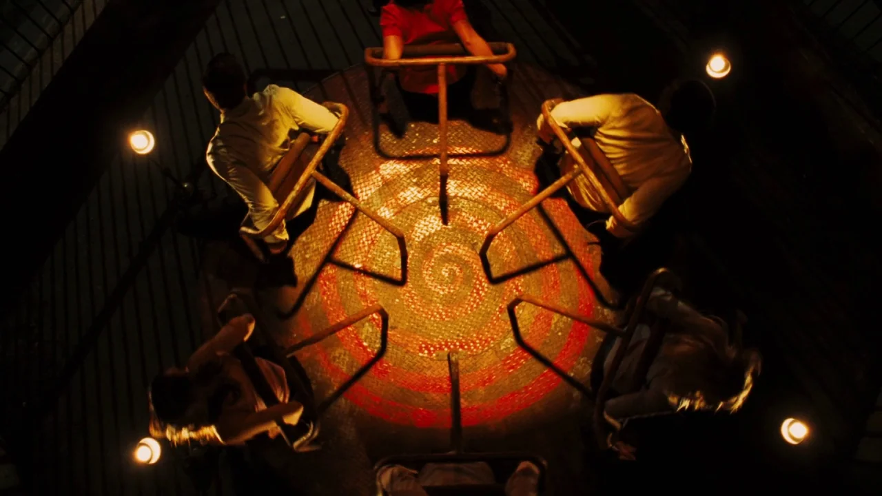Saw VI movie still: wide — A metal merry-go-round rotates on a dark outdoor playground at night. Five people sit on the perimeter of the ride under…