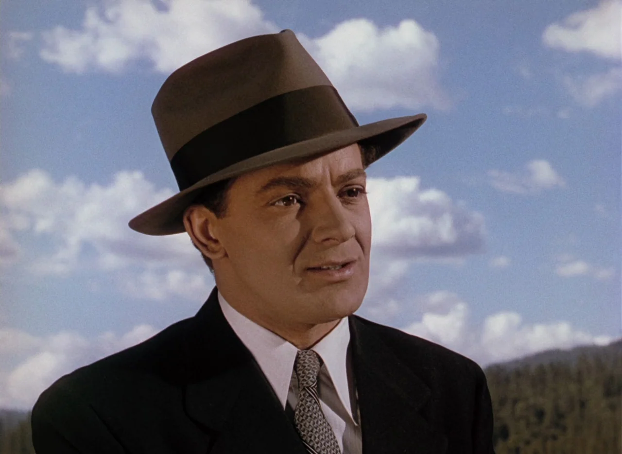 Leave Her To Heaven (1945) movie still: closeup — A man stands outdoors against a bright blue sky filled with scattered white clouds. The subject…