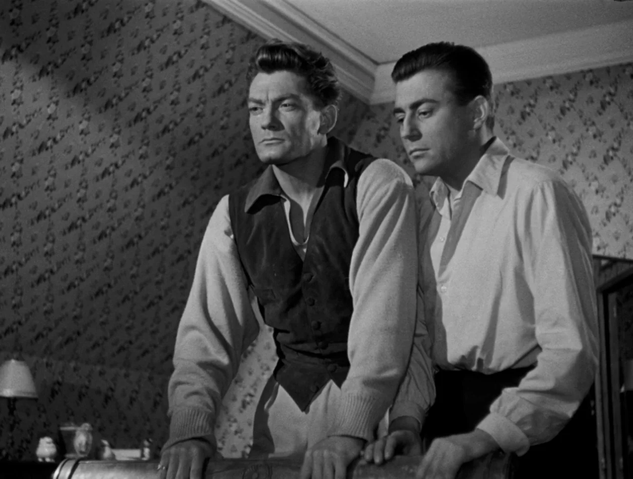 Orpheus (1950) movie still: medium — An interior space features patterned floral wallpaper and a lamp in the dim background. Two men lean forward…