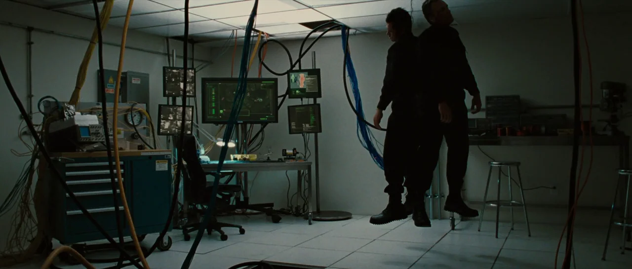 Iron Man 2 (2010) movie still: wide — A utilitarian server room features ceiling tiles, exposed cabling, and multiple active computer monitors. Two…
